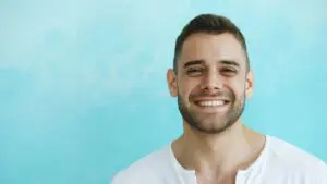 Photo by Vitaly Gariev: https://www.pexels.com/photo/smiling-man-in-white-shirt-against-blue-background-36813426/ Alt Text ID: Man smiling on a blue background 