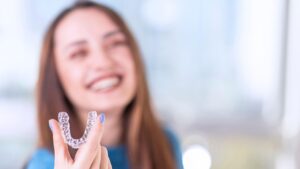 https://pixabay.com/photos/braces-dental-care-orthodontist-9055493/ Woman smiling holding Invisalign 